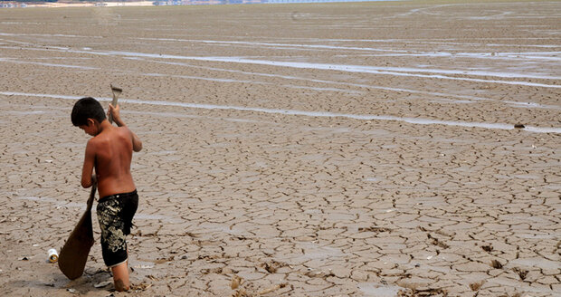 Boy carrying a paddle while walking through knee-high mud in a dried up river