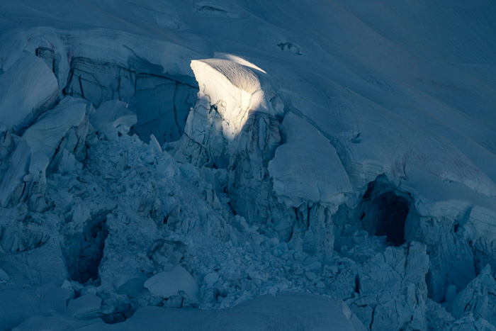 A glacier photographed in twilight, with a small cornice brightly illuminated