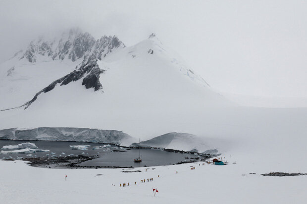 tourists walkinng along a ice-free inlet with towering snowbanks on the surrounding terrain