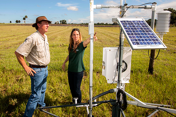 Two people stand in a field looking at a weather station