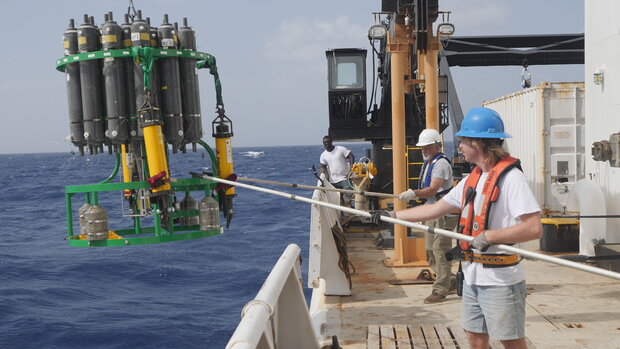 Photo of a scientist on the deck of a ship hauling in a CTD sampler